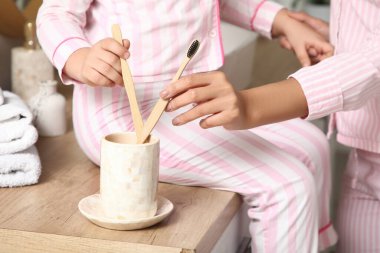 Küçük kız ve annesi banyoda diş fırçası ve pijama giyiyorlar.