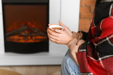 Oturma odasında şöminenin yanında çay bardağıyla güzel genç bir kadın, yakın çekim.