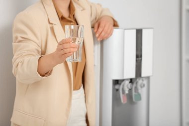 Ofisteki soğutucudan su içen genç bir kadın.