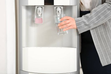 Woman pouring water from cooler into glass in office
