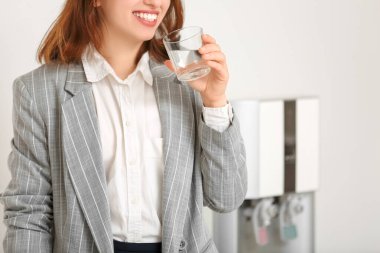 Ofisteki soğutucudan su içen gülümseyen genç kadın.