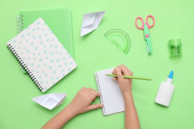 Çocuğun elleri yeşil arka plana not defterine bir şeyler yazıyor. Üst görünüm