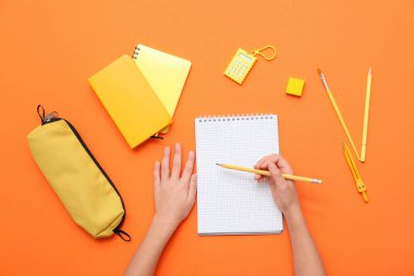 Çocuğun elleri turuncu arka planda deftere bir şey yazıyor. Üst görünüm
