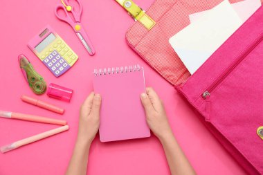 Pembe arka plandaki kırtasiye malzemelerinin arasında not defteri olan çocuk elleri. Üst görünüm