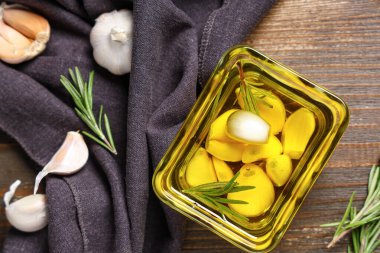 Ahşap zemin üzerinde biberiye bulunan bir kase taze sarımsak yağı.