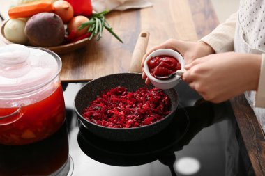 Genç bir kadın mutfakta lezzetli sebzeler pişirmek için domates ezmesi ekliyor.