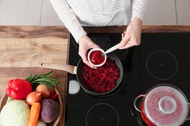 Genç bir kadın mutfakta leziz sebzeler pişirmek için domates ezmesi ekliyor.