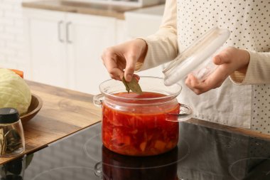 Çömleğe körfez yaprağı ekleyen genç bir kadın. Mutfakta leziz bir pancar çorbası, yakın plan.