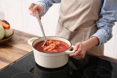 Mutfakta fırında çorba dolu bir tencereyle genç bir kadın, yakın plan.