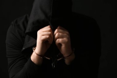 Elleri siyah arka planda kelepçeli genç adam yüzünü kapatıyor.