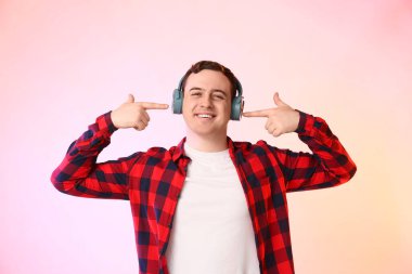 Renkli arka planda kulaklıkları işaret eden yakışıklı genç adam.
