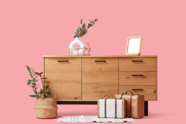 Okaliptüs dallı şık ahşap dolap, boş çerçeve ve pembe arka planda eski bavullar.