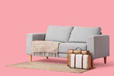 Şık gri kanepe ve pembe arka planda klasik bavullar.