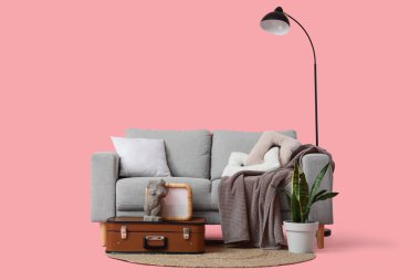 Ev bitkisi, boş çerçeve ve pembe arka planda klasik bavul olan şık gri kanepe.