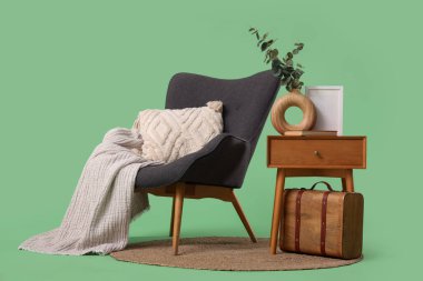 Yeşil arka planda şık gri koltuk, masa ve klasik bavul.