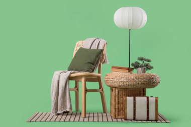 Hasır pouf, standart lamba ve yeşil arka planda klasik valizi olan şık bir sandalye.
