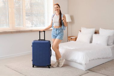 Otel odasında sırt çantalı ve bavullu bir kadın turist.