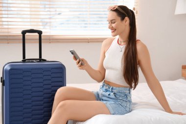 Otel odasında cep telefonu kullanan bavullu bir kadın turist.