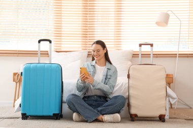 Otel odasında cep telefonu kullanan bavullu bir kadın turist.