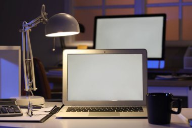Geceleri karanlık ofisteki masasında parlayan lamba olan boş bir laptop.