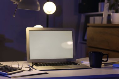 Geceleri karanlık ofisteki masada kahve fincanı olan boş bir laptop.