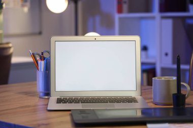 Kırtasiyeli ve kupalı boş bir dizüstü bilgisayar gece ofiste.