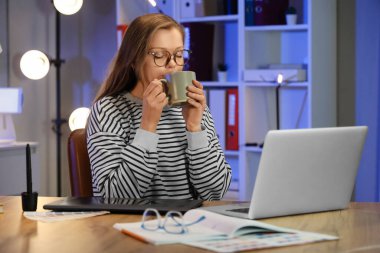 Kadın tasarımcı geceleri ofiste kahve içiyor.