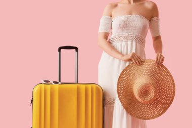 Pembe arka planda bavulu ve şapkası olan bir kadın turist.