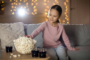 Evde film izlerken patlamış mısır yiyen tatlı küçük kız.