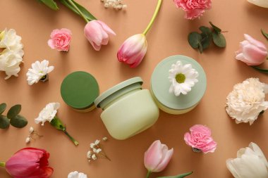 Farklı kozmetik kremler ve kahverengi arka planda güzel çiçekler.