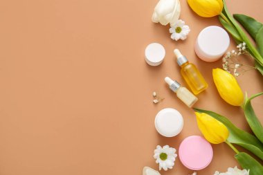 Farklı kozmetik ürünleri ve kahverengi arka planda güzel çiçekler.