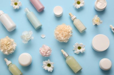 Farklı kozmetik ürünleri ve mavi arka planda güzel çiçekler.