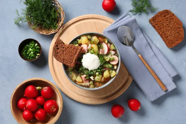 Bir kase lezzetli okroshka, malzemeler, ekmek ve kaşık ve gri arka planda.