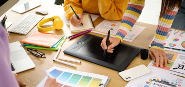 Grafik tasarımcılarından oluşan bir ekip masada tabletle çalışıyor, yakın plan.