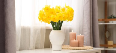 Masası, mumları ve narsisli çiçekleri olan şık bir oda.