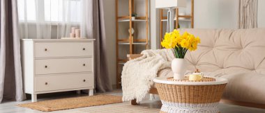 Kanepesi, çekmeceleri, sehpası ve narsisli çiçekleri olan şık bir oturma odası.