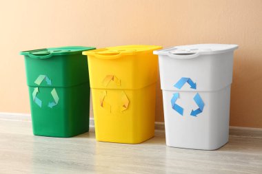 Bej duvarın yanında geri dönüşüm sembolü olan farklı çöp bidonları