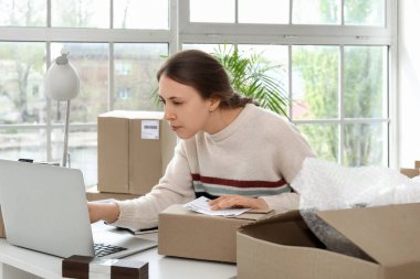 Ofiste dizüstü bilgisayar kullanan, paketli genç bir kadın.