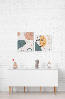 Beyaz tuğla duvarın yanında farklı resimler olan şık bir dolap.