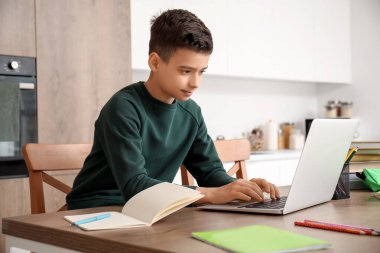 Küçük çocuk mutfakta dizüstü bilgisayarla online çalışıyor.