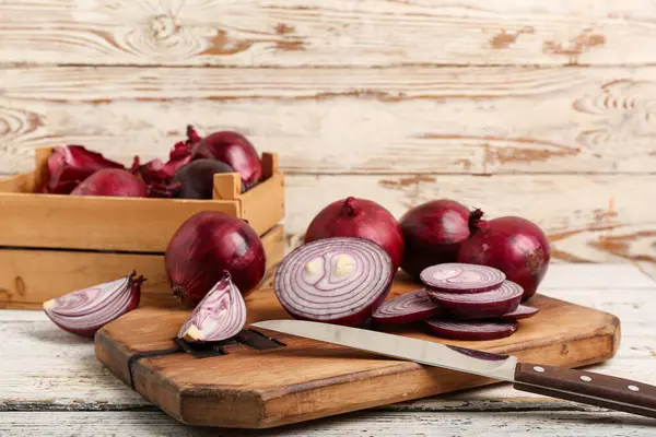 Beyaz ahşap arka planda taze kesilmiş kırmızı soğan ve kutu.