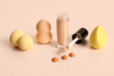 Bir şişe makyaj malzemesi ve sarı arka planda süngerler.