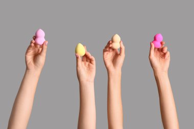 Gri arka planda farklı makyaj süngerleri olan kadın elleri