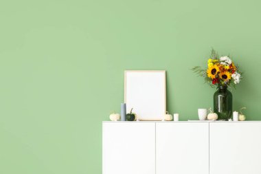 Sonbahar çiçeği buketli beyaz büfe, boş çerçeve ve yeşil duvarın yanında balkabakları