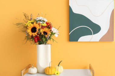 Sonbahar çiçekleri ve turuncu duvarın yanında balkabakları olan raf ünitesi.