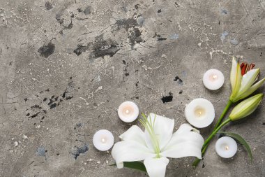 Güzel zambak çiçekleri ve gri arka planda yanan mumlar