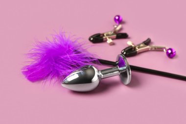 Tüy çubuğu, meme ucu kıskaçları ve mor arka plandaki seks dükkanının anal tıpası.
