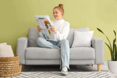 Young woman reading newspaper on sofa at home
