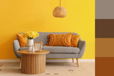 Masada nergis çiçekli vazo ve oturma odasında gri kanepe. Farklı renk desenleri