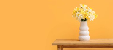 Turuncu arka planda narsist çiçekli vazo.